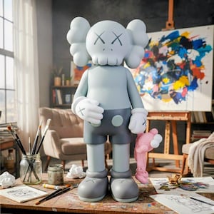 Puede incluir: Una figura KAWS Companion gris claro con ojos tachados y una cabeza en forma de calavera. Viste pantalones cortos grises, guantes y zapatos, sosteniendo un juguete de peluche rosa. La figura est&aacute; sobre una mesa de madera con materiales de arte.