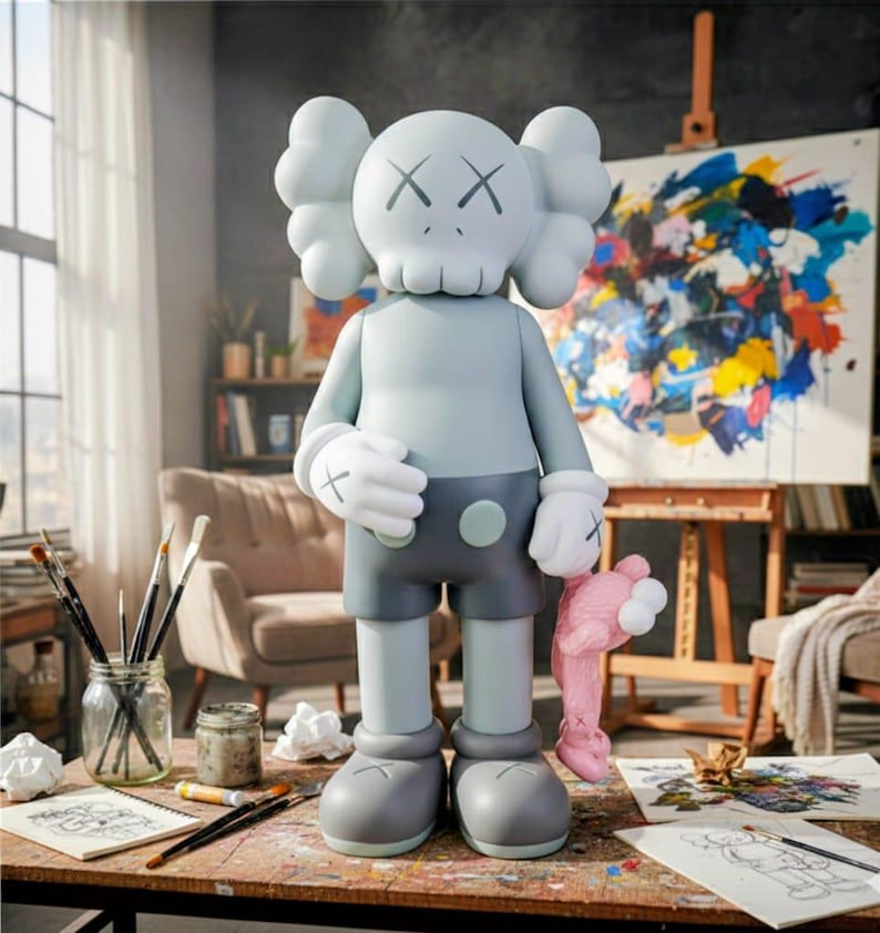 Puede incluir: Una figura KAWS Companion gris claro con ojos tachados y una cabeza en forma de calavera. Viste pantalones cortos grises, guantes y zapatos, sosteniendo un juguete de peluche rosa. La figura est&aacute; sobre una mesa de madera con materiales de arte.