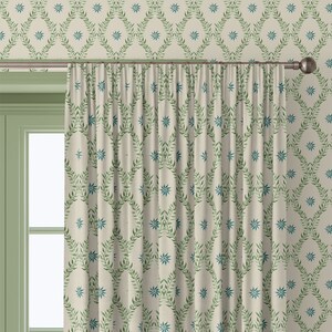 May include: A pair of cream-coloured curtains with a green and blue floral pattern. The curtains are hung on a metal rod and are partially drawn, revealing a green wall with a similar floral pattern.