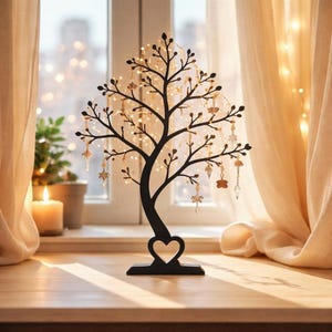 Peut inclure: Un présentoir à bijoux en métal noir en forme d'arbre, avec une base en forme de cœur. Les branches sont ornées de petits ornements et de guirlandes lumineuses. Il est posé sur une surface en bois près d'une fenêtre.