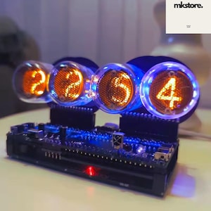 May include: A digital clock with four glowing orange digits: 2, 2, 5, and 4. The numbers are displayed in clear glass tubes, mounted on a black circuit board base with blue LED lights. The clock has the text "mkstore." in the upper right corner.