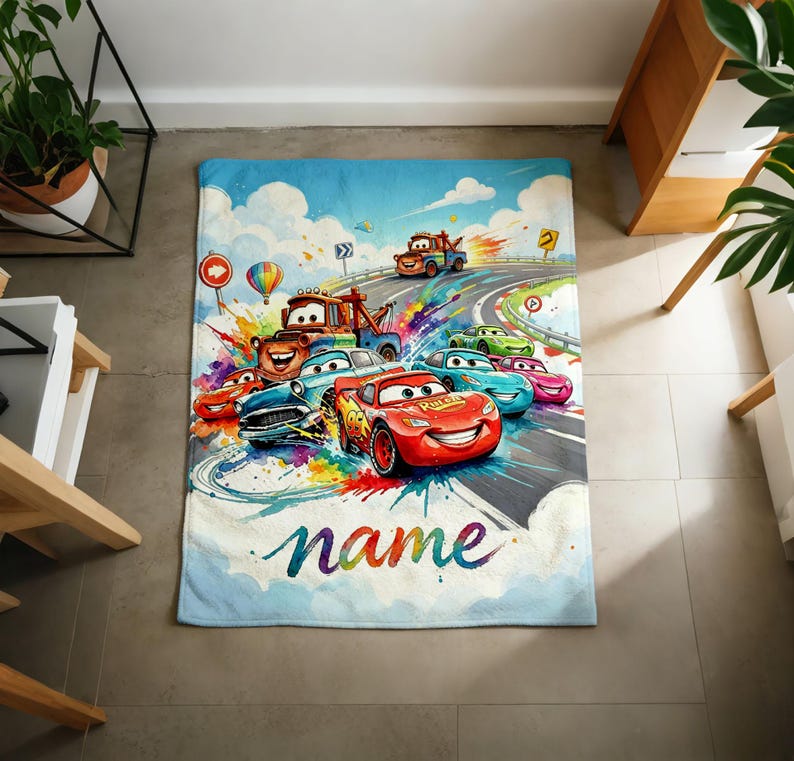 Puede incluir: Una colorida manta con tem&aacute;tica de Cars que presenta a Rayo McQueen y otros personajes corriendo en una pista. El dise&ntilde;o incluye un cielo azul, una carretera y la palabra "name" en colores arco&iacute;ris. La manta es rectangular.