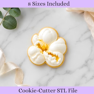 May include: A cookie shaped like a popcorn kernel with white icing and yellow accents. The text 8 Sizes Included and Cookie-Cutter STL File is displayed at the top and bottom of the image, indicating a digital file for a cookie cutter.