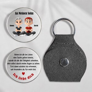 May include: A personalized keychain set featuring two round metal pendants and a leather holder. One pendant reads "An Meinen Sohn" with cartoon figures and names. The other pendant has a German message and a heart.