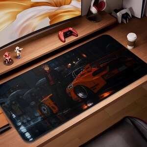 May include: A large rectangular desk mat featuring a vibrant anime-style illustration of a car and character in a rainy urban setting. The car is orange with the text "Liberty Walk". The mat is designed for gaming or office use.