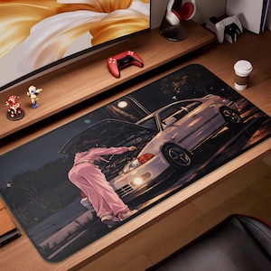 May include: A black desk mat featuring a nighttime anime scene with a white car and a person in pink clothing working on the engine. The mat has a rectangular shape and is designed for a desk.