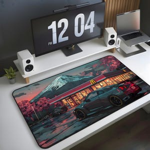 May include: A large rectangular desk mat featuring a vibrant anime-style illustration. The design showcases a car parked in front of a restaurant with a mountain backdrop. The color palette includes shades of blue, red, and orange.
