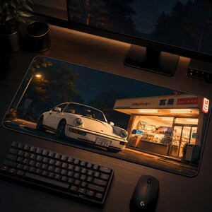 May include: A rectangular desk mat featuring a printed scene of a white sports car parked at night in front of a brightly lit Japanese convenience store. The store facade displays Japanese text and a red sign, while the car has a license plate reading 071.