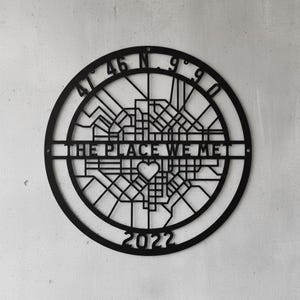 Könnte beinhalten: Schwarze Metall-Wandkunst mit einem Stadtplan-Design. Das Kunstwerk enthält den Text "THE PLACE WE MET" und das Jahr "2022". Koordinaten sind oben dargestellt. Eine Herzform ist in die Karte integriert.