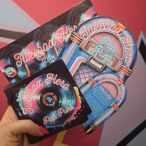May include: A selection of Jukebox Hero Pop Punk themed items. The items include a stack of black cards with a vinyl record design and the text "Jukebox Hero Pop Punk". There are also two jukebox-shaped cards with the same text.