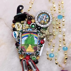 Puede incluir: Un collar caprichoso con elementos de El Mago de Oz. Incluye un sombrero de bruja negro, una imagen de la Ciudad Esmeralda, zapatillas rojas y una imagen de los personajes. El collar está adornado con gemas de colores y una cadena dorada.