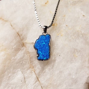 May include: A silver chain necklace with a blue opal pendant shaped like the state of Michigan.