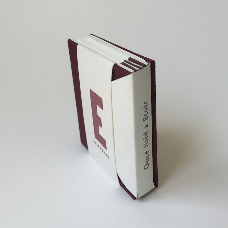 May include: A small burgundy book with a white spine. The spine has the text "Once Said a Stoic" and the letter "E" for Epictetus.