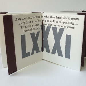 May include: A small, white book with a brown spine. The book is open to reveal a page with the text "AND ARE ALL profited by what they hear? So it seems there is an art of hearing as well as of speaking.... To make a statue needs skill also. needs skill: to view a statue LXXXI" printed in black. The page is decorated with a large, gray number "LXXXI" printed in a bold font.
