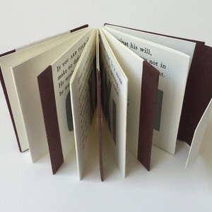 May include: A small, burgundy-bound book with white pages. The book is open, revealing the text "IF YOU ARE TOLD make no det He surg he wa inst his will, not in at."