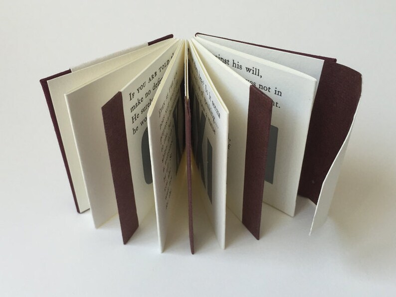 May include: A small, burgundy-bound book with white pages. The book is open, revealing the text "IF YOU ARE TOLD make no det He surg he wa inst his will, not in at."