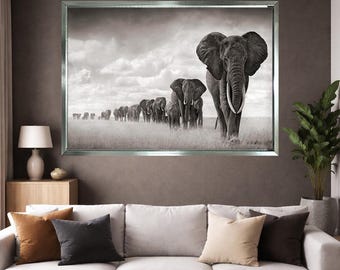 May include: Black and white framed print of a herd of elephants walking across a grassy field. The lead elephant is large with prominent tusks. The sky is overcast, and the print is displayed above a white sofa.