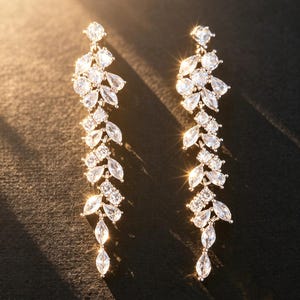 May include: A pair of elegant, dangling earrings. Each earring features a cascade of clear, sparkling crystals in various shapes, including round and teardrop. The crystals are set in a silver-toned metal, creating a glamorous and eye-catching accessory.