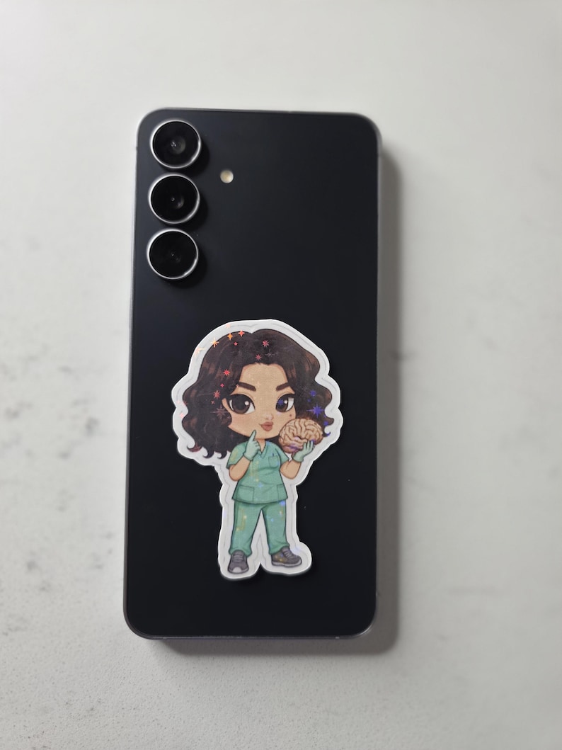 Puede incluir: Una pegatina de una enfermera de dibujos animados sosteniendo un cerebro, colocada en un tel&eacute;fono inteligente negro. La enfermera lleva un uniforme verde y tiene el pelo rizado oscuro. La pegatina tiene un borde blanco y un fondo gris claro.