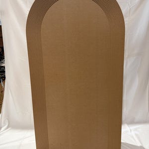 May include: A large, arched wooden panel in a warm brown colour. The top edge features a series of parallel, curved grooves, creating a layered effect. The panel has a smooth, flat surface, suitable for various decorative or functional uses.