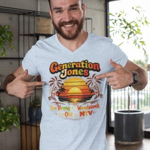 May include: Light blue v-neck t-shirt with a retro graphic design. The design features the text "Generation Jones" in orange and yellow, with a sunset scene and palm trees. Below the main text are the words "Too Young for Woodstock, Too Old for MTV."