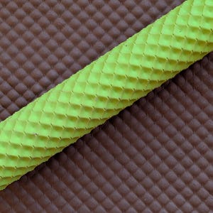 May include: Close-up of a textured, neon green object with a diamond pattern, set against a brown, diamond-patterned background. The object appears to be a rolled material, possibly for crafting or design purposes.