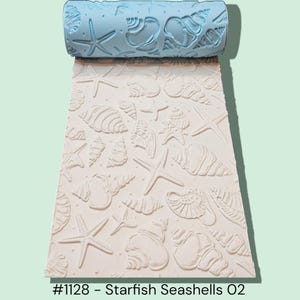 May include: A light blue textured paint roller with a repeating pattern of seashells and starfish. The roller is shown rolled out on a white surface, displaying the embossed design. The text "#1128 - Starfish Seashells O2" is visible.