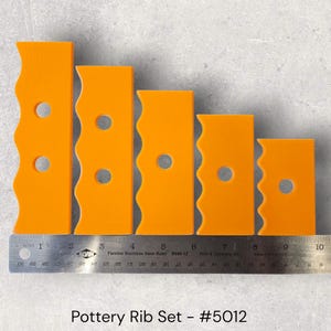 May include: Five orange pottery ribs with a wavy edge and a circular hole are displayed. A metal ruler with centimetre measurements is placed below the ribs. The text "Pottery Rib Set - #5012" is at the bottom.