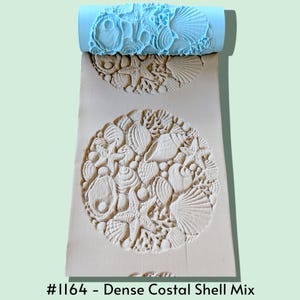 May include: A light blue cylindrical clay texture roller featuring a raised pattern of various seashells, starfish, and coral. The roller is shown pressing into a flat piece of beige clay, leaving a detailed, repeating impression of the marine life.