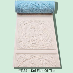 May include: A light blue textured roller with a koi fish design, used to create an embossed pattern on a white surface. The embossed pattern features two koi fish and swirling water. The text at the bottom reads "#1124 - Koi Fish O1 Tile."