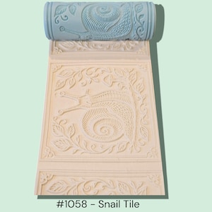 May include: A light blue roller with a snail design is shown above a cream-colored tile with a matching snail and leaf pattern. The tile is rectangular with a border. The text "#1058 - Snail Tile" is at the bottom.