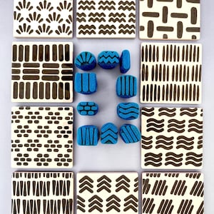 May include: A collection of nine square ceramic tiles featuring various black geometric patterns on a cream background, accompanied by ten small blue foam stamps with matching patterns arranged in the center of the layout.