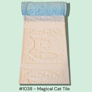 May include: A light blue patterned roller with a cream-colored embossed design of a cat face and floral elements. The text "#1038 - Magical Cat Tile" is at the bottom of the image. The roller is designed for creating decorative patterns.