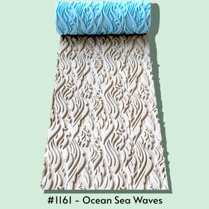 May include: A light blue patterned texture roller positioned above a white clay slab embossed with a repeating ocean sea waves design. The roller features a raised wave motif that creates a continuous impression, labeled as #1161 - Ocean Sea Waves.