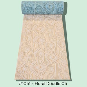 May include: A light blue floral pattern rolling pin with a matching embossed design on the rolled-out surface. The pattern features various flower shapes and textures. The text "#1051 - Floral Doodle 05" is visible at the bottom.