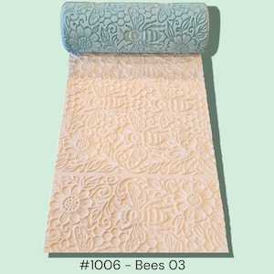 May include: A light blue rolling pin with a bee and floral pattern, resting on a sheet of embossed paper with a matching design. The paper is off-white, and the text "#1006 - Bees O3" is at the bottom.