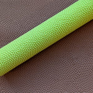 May include: A close-up of a neon green cylindrical object with a textured surface. The object is set against a brown, textured background. The object appears to be a roll of material.