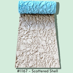 May include: A light blue cylindrical patterned rolling pin with a textured surface featuring a variety of embossed seashells. The roller has imprinted a beige clay sheet with the same shell pattern. The text #1167 - Scattered Shell is visible.