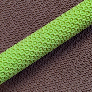 May include: A close-up shot of a textured, lime green cylindrical object with a honeycomb pattern. It is set against a brown background with a repeating circular design, creating a contrast in colour and texture.