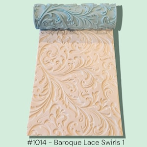 May include: A light blue cylindrical rolling pin with a raised, intricate baroque lace swirl pattern. The roller is positioned above a white rectangular sheet of material that displays the same embossed, flowing, and ornate floral-inspired design.