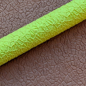 May include: A close-up shot of a textured, neon green cylindrical object. The object has a repeating pattern of raised, irregular shapes. The background is a brown, textured surface with a similar pattern.