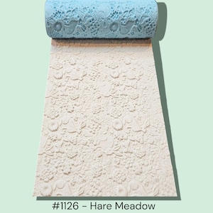 May include: A light blue rolling pin with a floral design is rolled out on a white surface with a matching embossed floral pattern. The text "#1126 - Hare Meadow" is at the bottom.