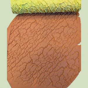 May include: A cylindrical lime green textured rolling pin positioned above a flat sheet of terracotta-colored clay. The clay surface features a deep, intricate, and irregular cracked pattern that has been imprinted by the rolling tool above it.