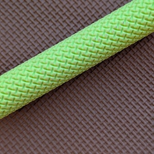 May include: A close-up of a bright green, cylindrical object with a woven texture. It's set diagonally against a brown, textured background, creating a contrast in colour and texture. The object appears to be a handle or grip.