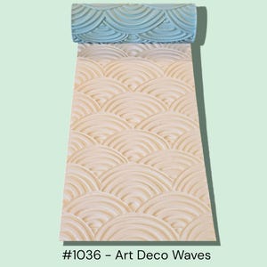May include: A decorative roller with an Art Deco wave pattern. The roller is light blue at the top and transitions to a beige color, creating a textured, repeating fan-like design. The text "#1036 - Art Deco Waves" is at the bottom.