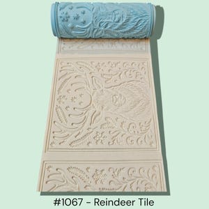 May include: A light blue patterned roller and a cream-colored tile with a reindeer design. The roller has a snowflake and reindeer pattern. The tile features a detailed embossed reindeer and floral design. The text at the bottom reads "#1067 - Reindeer Tile."