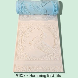 May include: A light blue patterned roller and a cream-colored tile with a hummingbird design. The tile has a circular frame with an ornate border. The text "#1107 - Humming Bird Tile" is at the bottom.