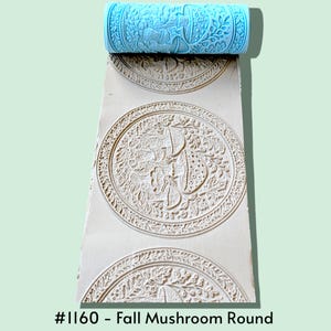 May include: A light blue cylindrical rolling pin with a raised pattern of mushrooms and foliage, shown pressing a repeating circular design into a flat beige surface. The text #1160 - Fall Mushroom Round is printed at the bottom of the image.