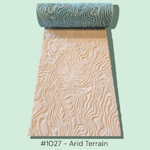 Peut inclure: Un rouleau texturé bleu clair avec un motif de terrain aride crème. Le motif est estampé sur une surface crème. Le texte "#1027 - Arid Terrain" est au bas de l'image. Cet outil est probablement utilisé pour l'artisanat ou la décoration.