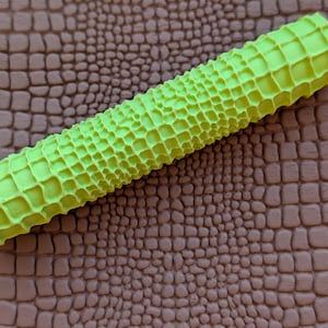 May include: A bright neon green textured roller with a honeycomb pattern is set against a brown, faux-leather background. The roller's design suggests a crafting or DIY theme, possibly for embossing or texturing.